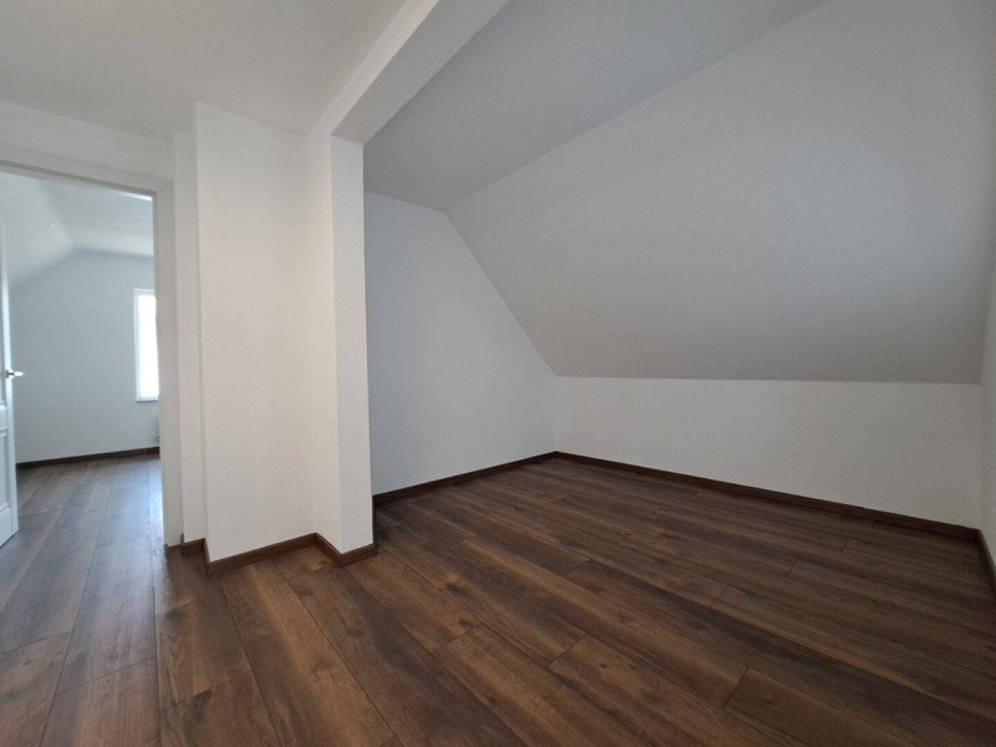 Helles Dachzimmer mit Holzboden und schrägen Wänden, ideal als Gästezimmer oder Büro.