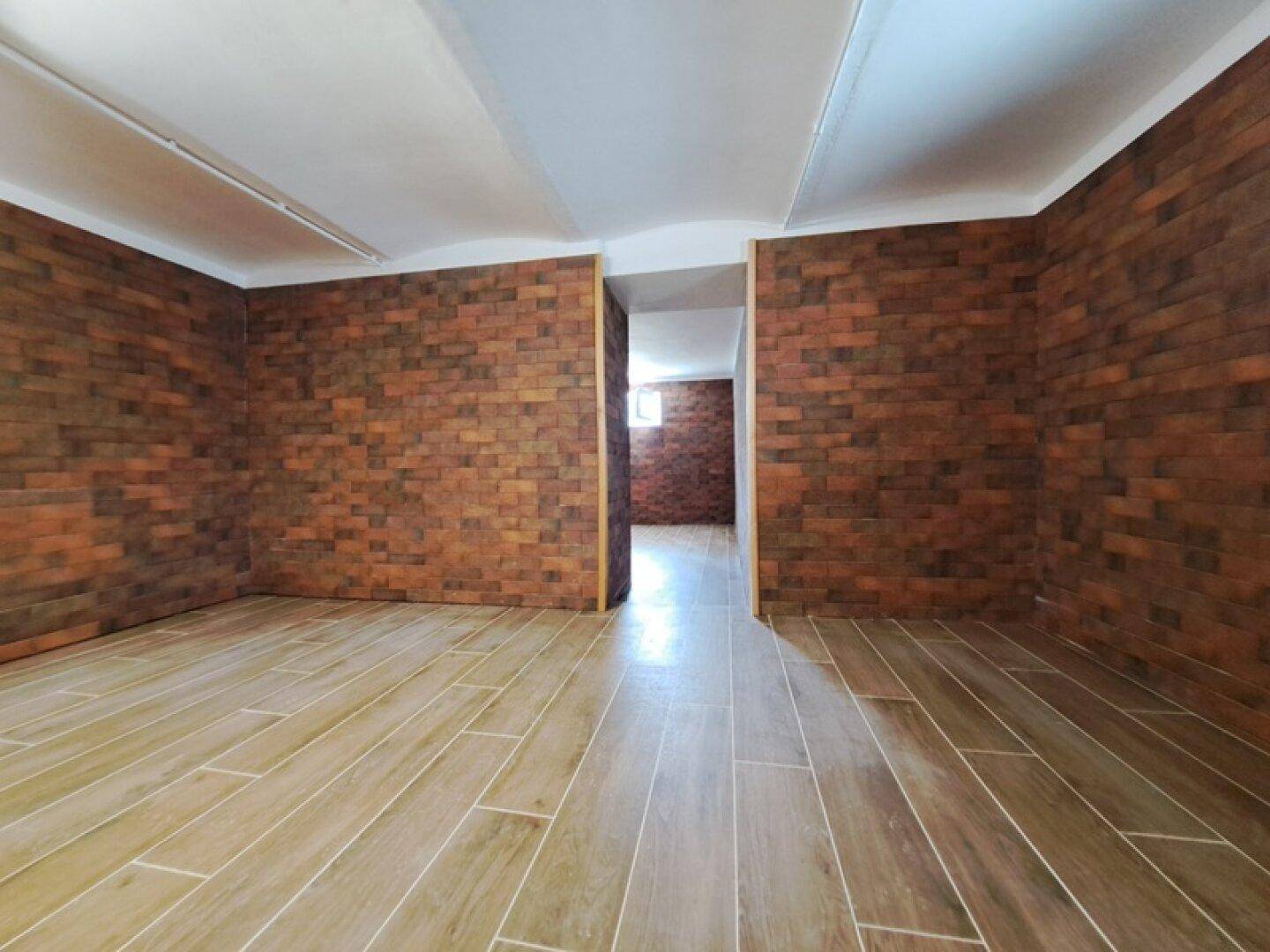 Geräumiger Kellerraum mit Ziegelwandverkleidung und Fliesenboden, vielseitig nutzbar.