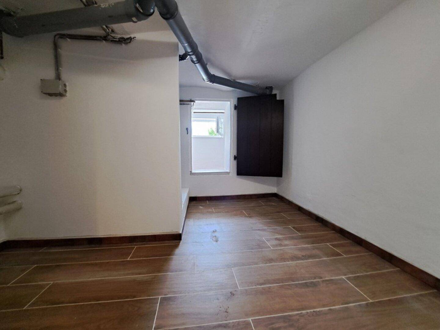 Praktischer Hauswirtschaftsraum im Keller mit Fliesenboden und Fenster, ideal für Lagerung.