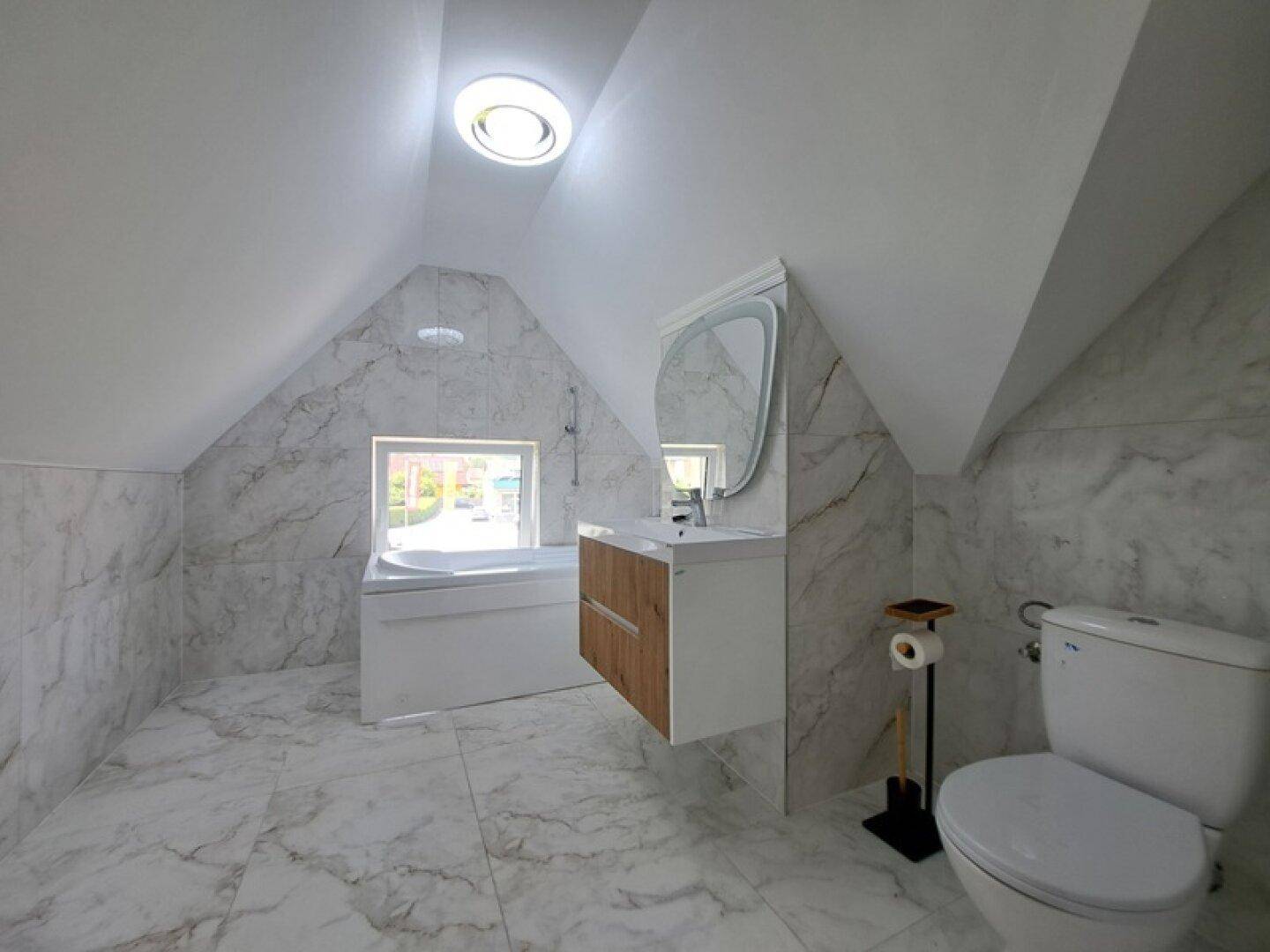 Modernes Dachbad mit Marmorfliesen, Badewanne, Waschtisch und Dachfenster für Helligkeit.