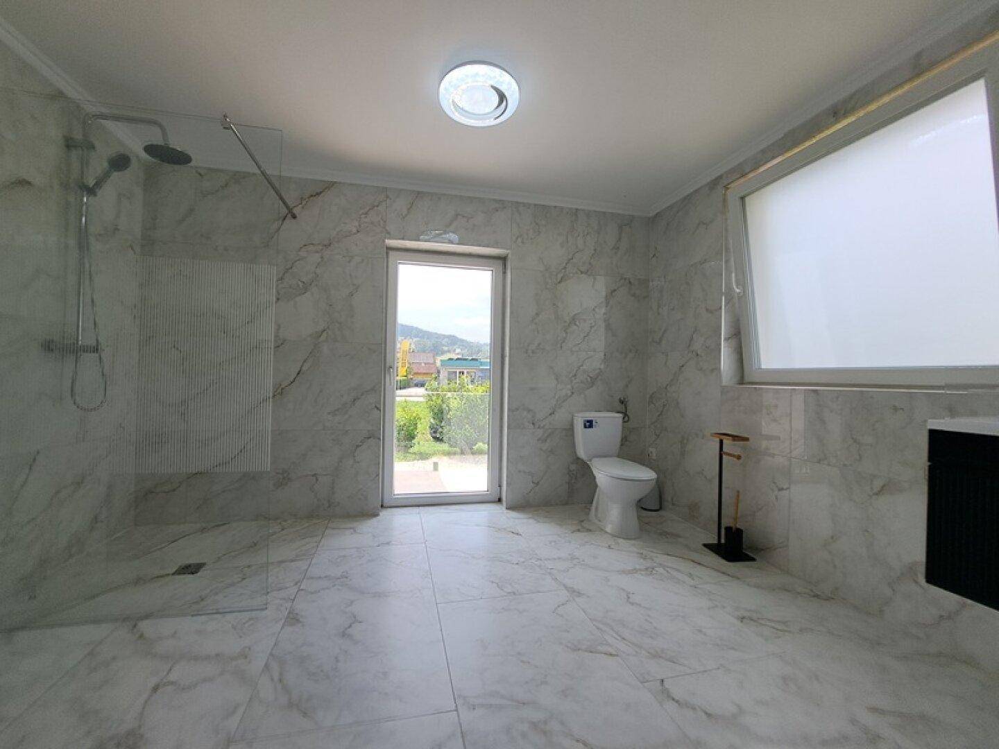 Geräumiges Badezimmer mit modernen Marmorfliesen, ebenerdiger Dusche und Fenster mit Ausblick.