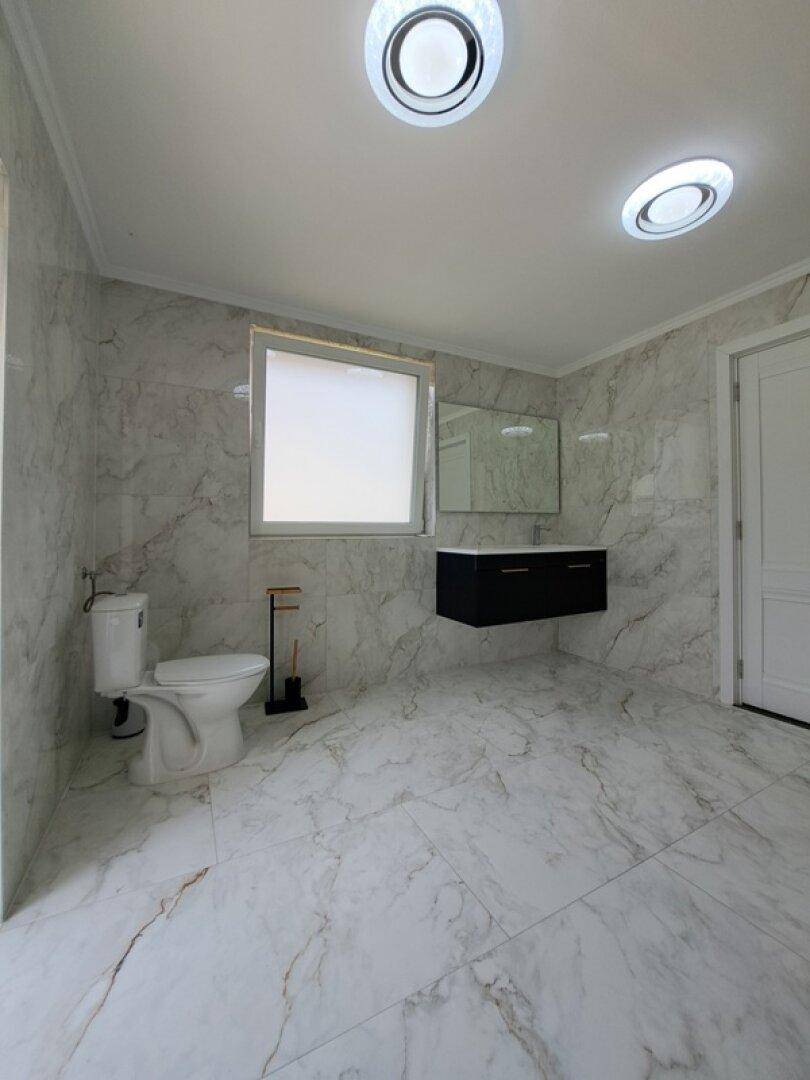 Modernes Badezimmer mit Marmorfliesen, schwebendem Waschtisch und großem Spiegel über dem Waschbecken.