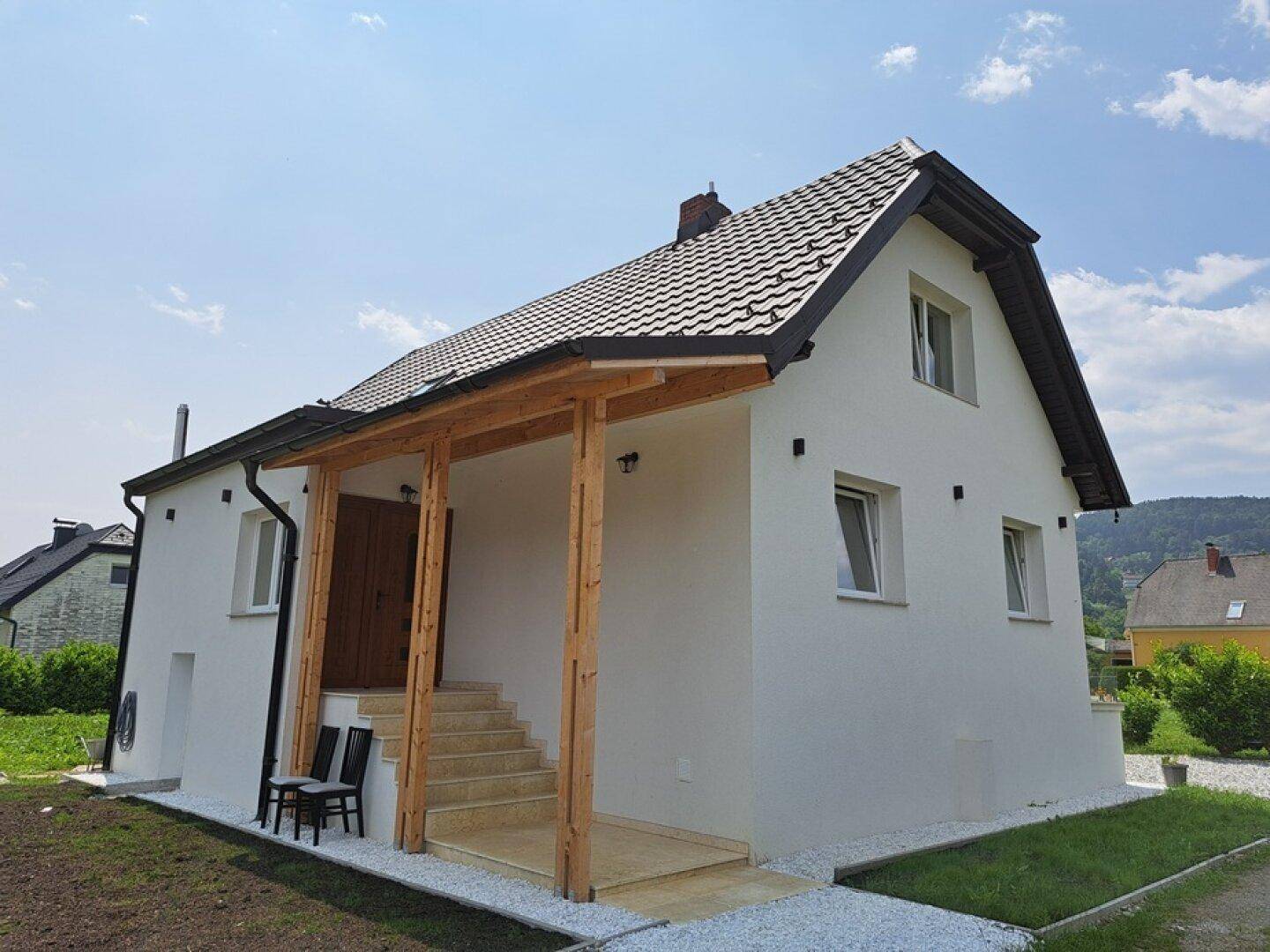 Weißes Einfamilienhaus mit überdachtem Eingangsbereich und Satteldach unter blauem Himmel.