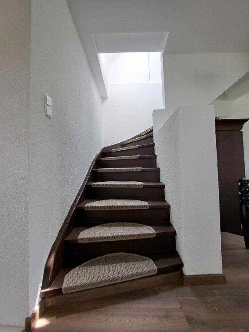 Geschwungene Holztreppe mit Teppichstufen und hellem Treppenhaus, das nach oben führt.