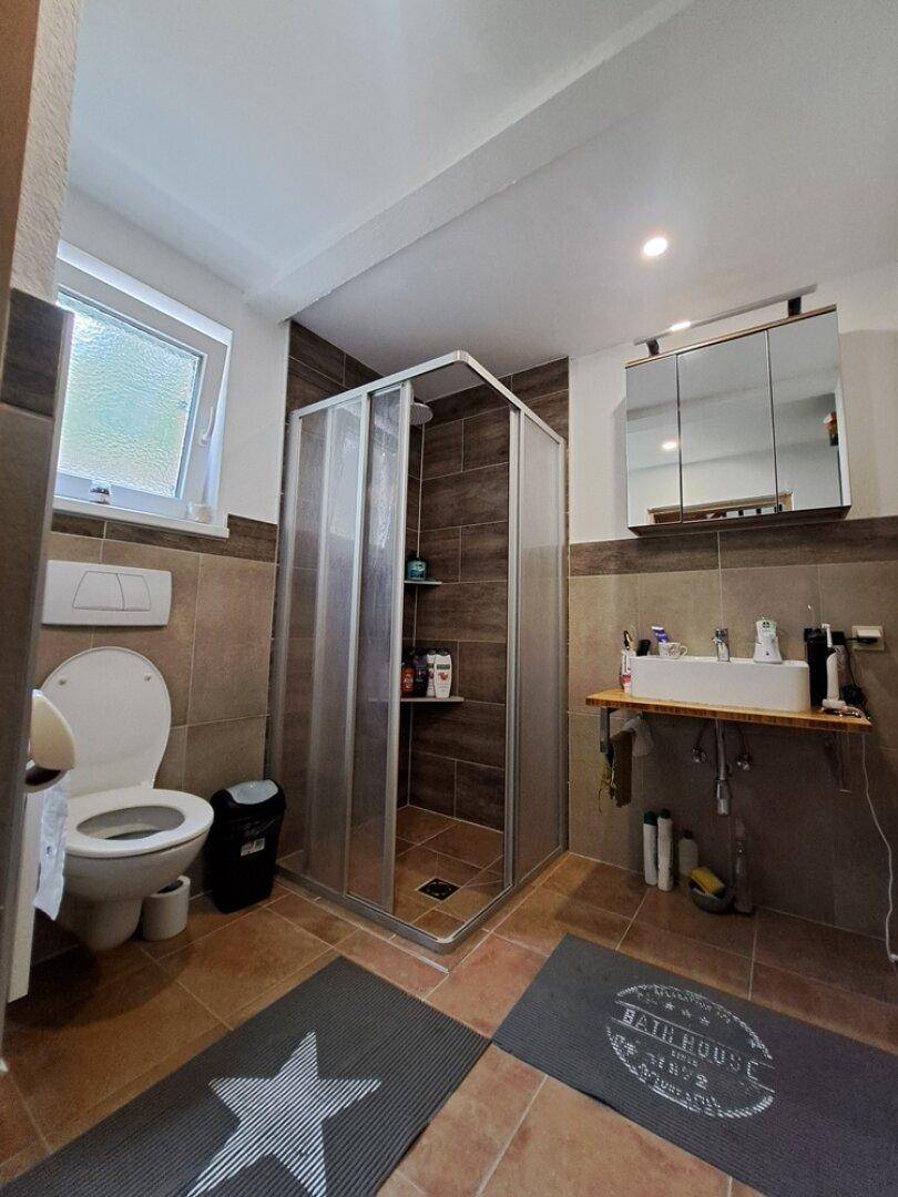 Funktionales Badezimmer mit Duschkabine, WC, Einzelwaschbecken und Spiegelschrank, gefliest in Brauntönen.