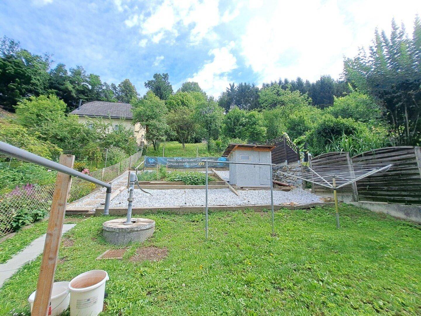 Gepflegter Gartenbereich mit kleiner Hütte, Wasserpumpe und Wäscheleine, umgeben von viel Grün.