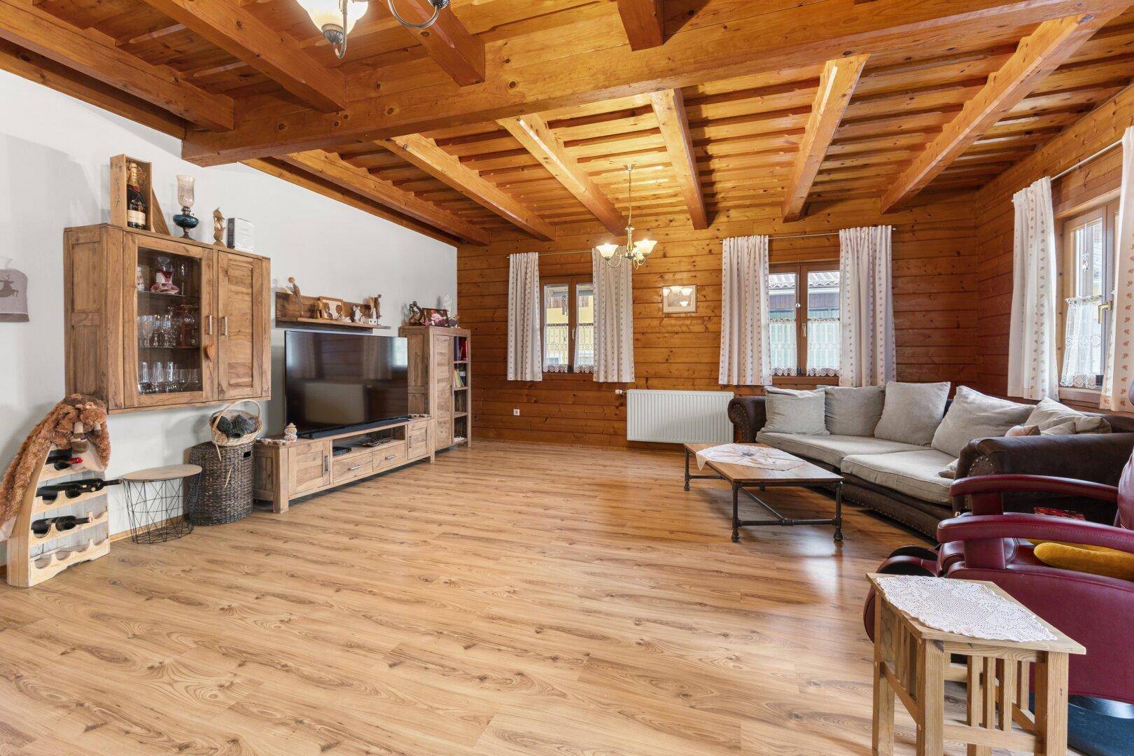 Rustikales Wohnzimmer mit Holzwänden, Holzbalkendecke, Laminatboden und traditionellen Holzmöbeln.