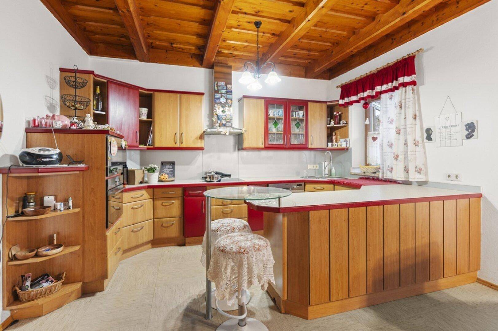 Traditionelle Küche mit Holzschränken, roten Akzenten, Frühstücksbar und gemütlichem Essbereich.