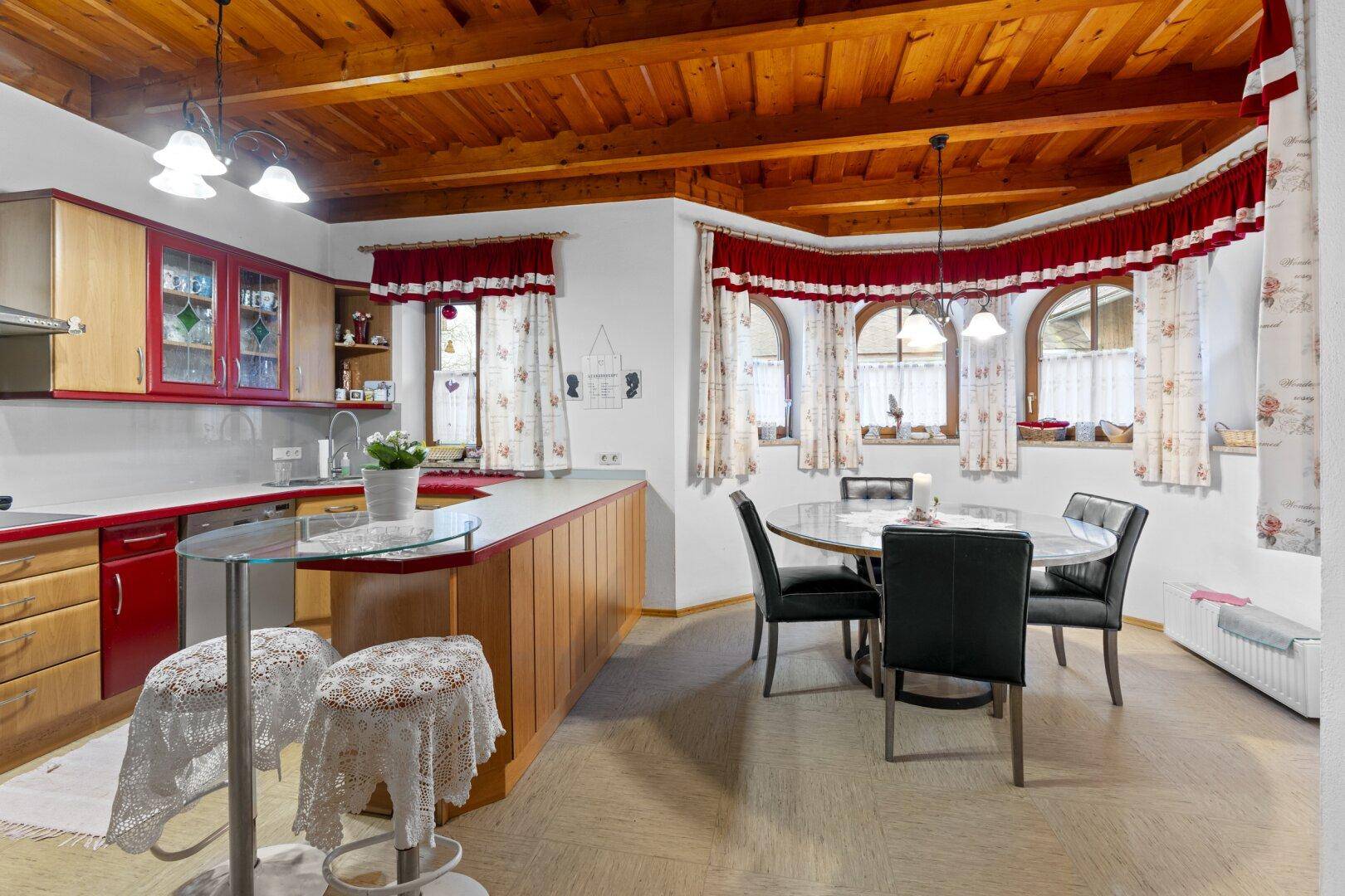 Geräumige Küche mit Holzmöbeln, roten Details, Frühstücksbar und einem separaten Essbereich.
