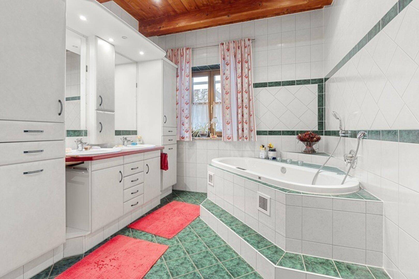 Badezimmer mit grünen und weißen Fliesen, einer Eckbadewanne und einem Fenster.