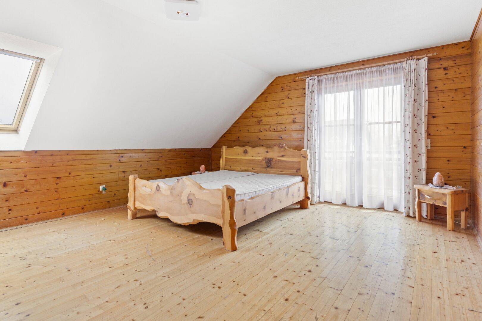 Gemütliches Schlafzimmer im Dachgeschoss mit Holzwänden, Dachschräge und einem Holzbett.