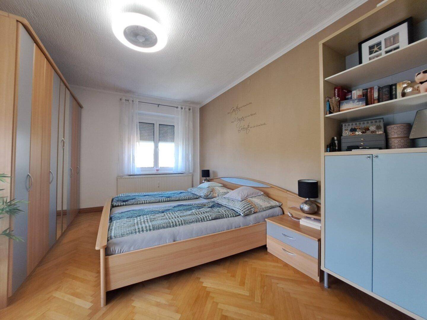 Geräumiges Schlafzimmer mit Doppelbett, großem Kleiderschrank und Parkettboden, freundlich und funktional eingerichtet.