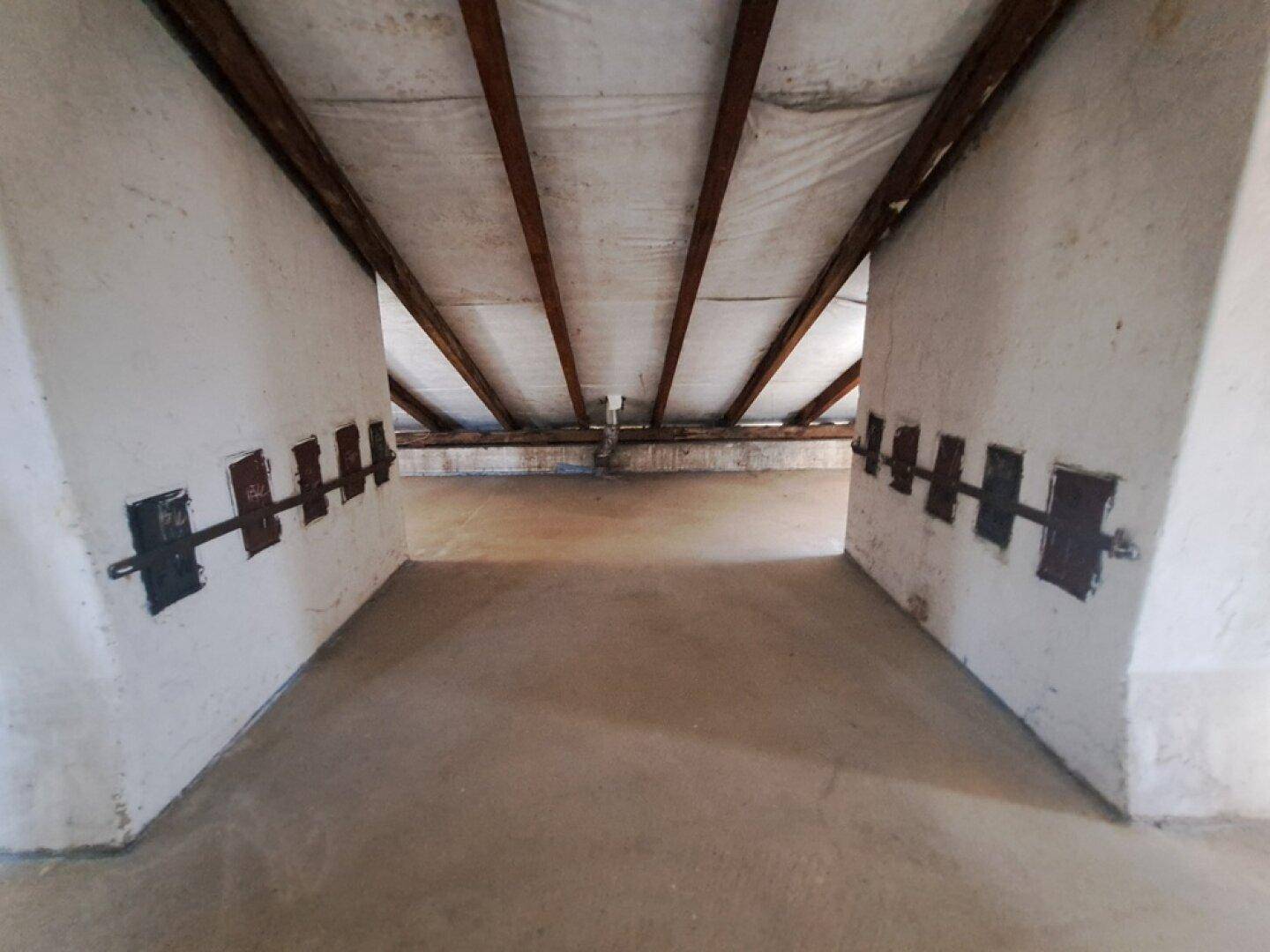 Unausgebauter Dachboden mit sichtbaren Holzbalken und Betonboden, bietet Potenzial für Ausbau.