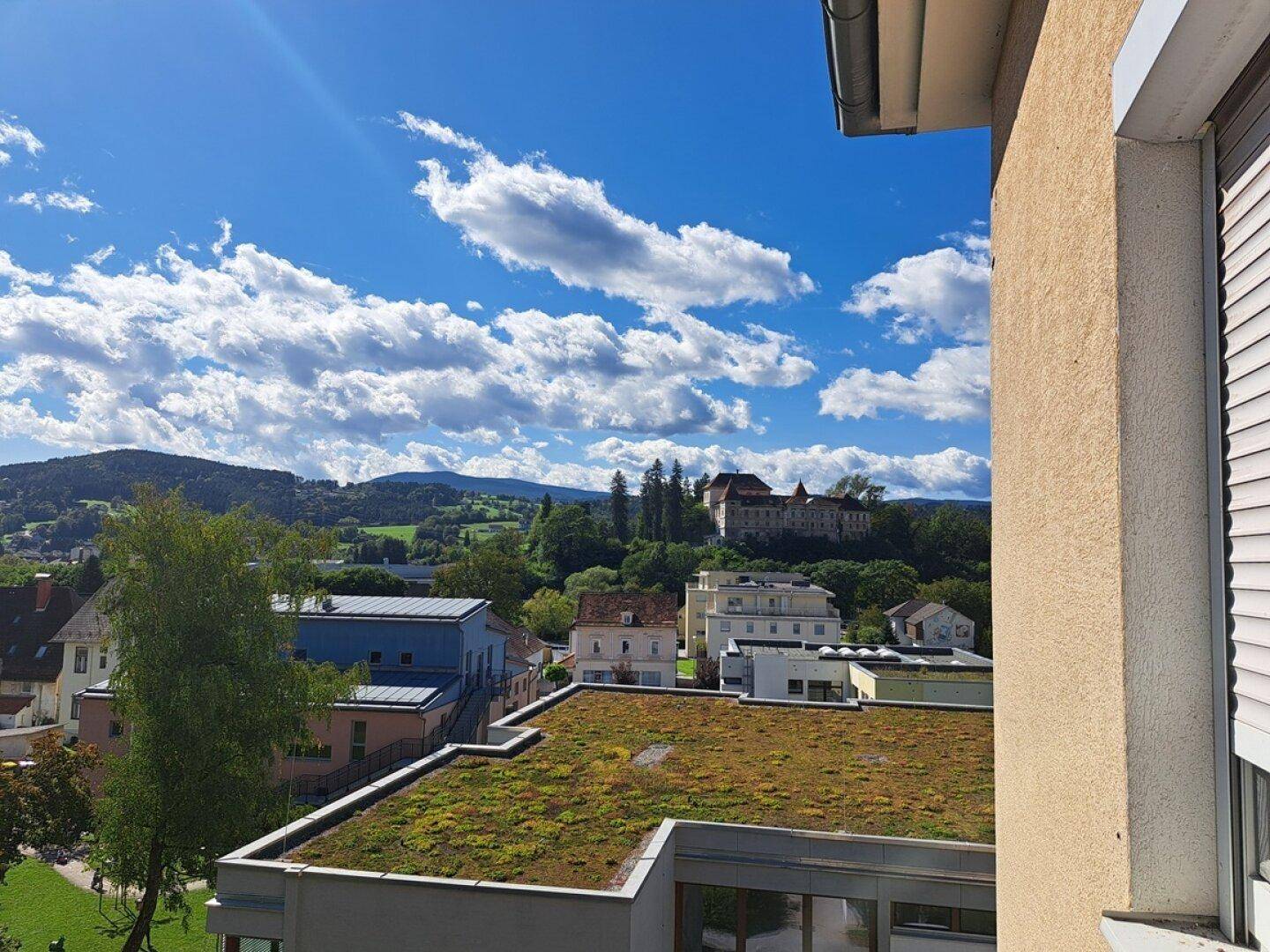 Weitblick über die Landschaft mit einem Schloss auf einem Hügel und einem Gebäude mit begrüntem Dach im Vordergrund.