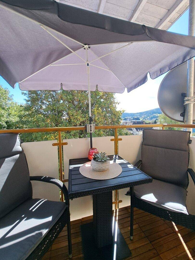 Gemütlicher Balkon mit Gartenmöbeln und Sonnenschirm, ideal zum Entspannen mit grüner Aussicht.