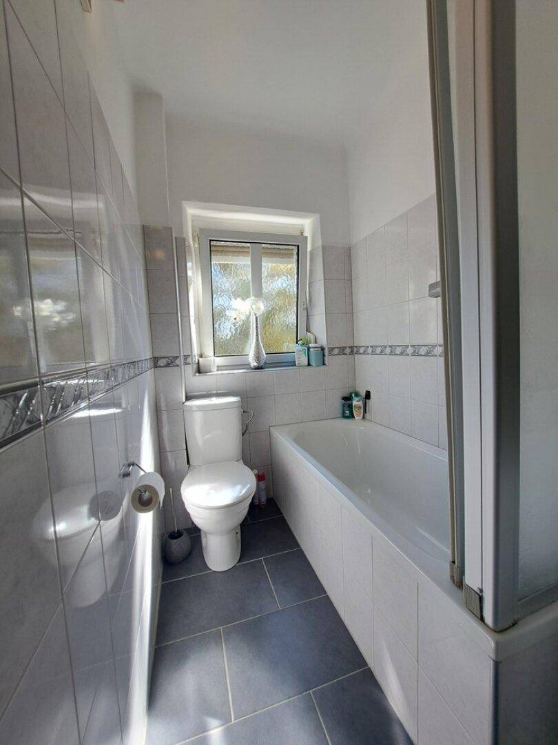 Helles Badezimmer mit Badewanne, WC und Fenster, komplett gefliest für einfache Pflege.