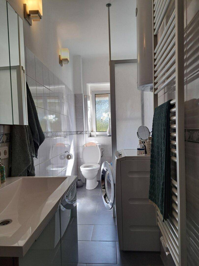 Modernes Badezimmer mit Waschbecken, WC, Waschmaschine und beheiztem Handtuchhalter, hell gefliest.