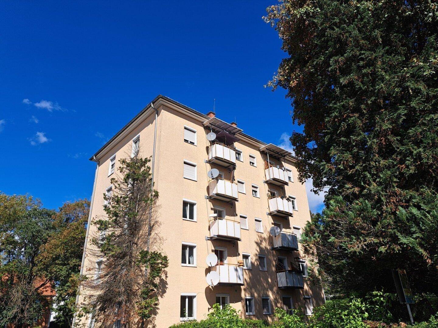 Mehrstöckiges Wohngebäude mit zahlreichen Balkonen und Solaranlagen auf dem Dach unter blauem Himmel.