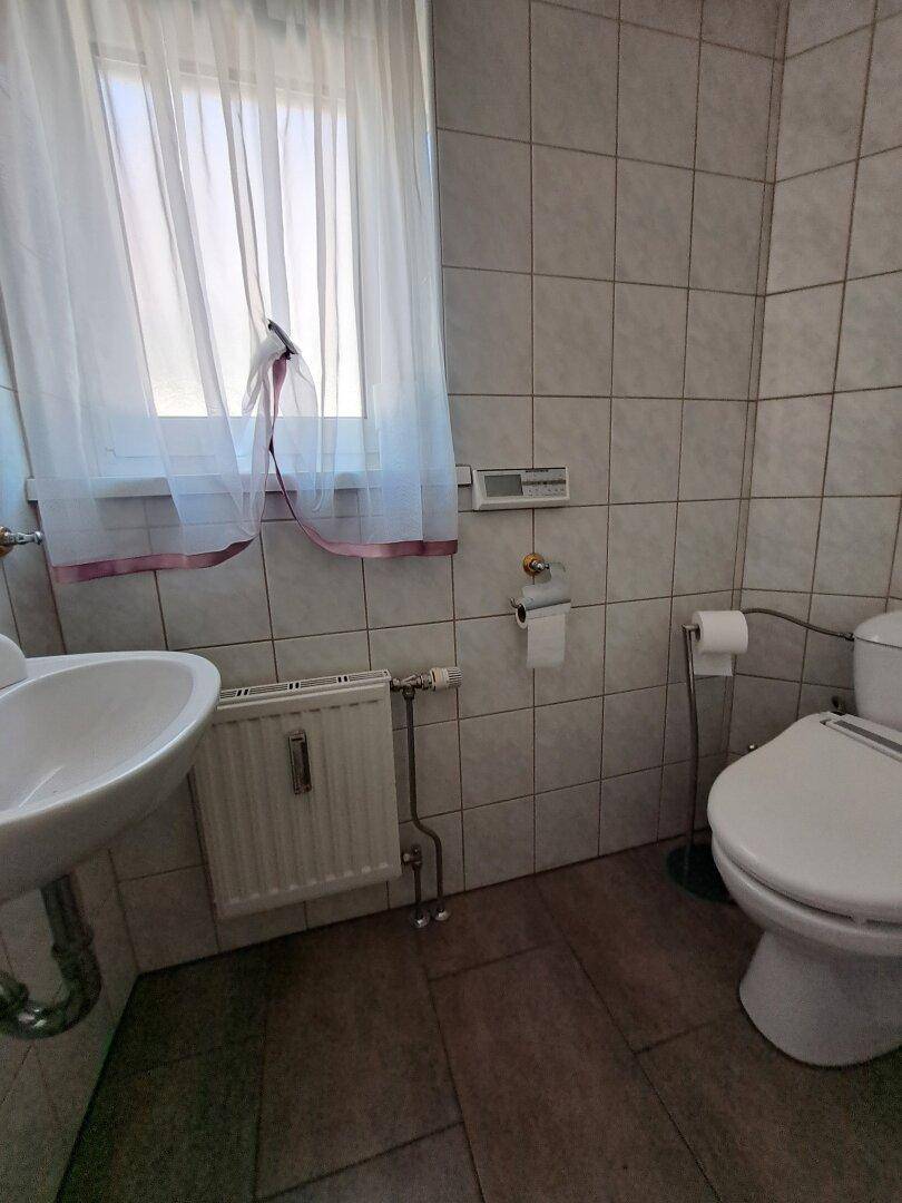 Kleines Gäste-WC mit Fenster, Fliesenboden und Heizkörper.