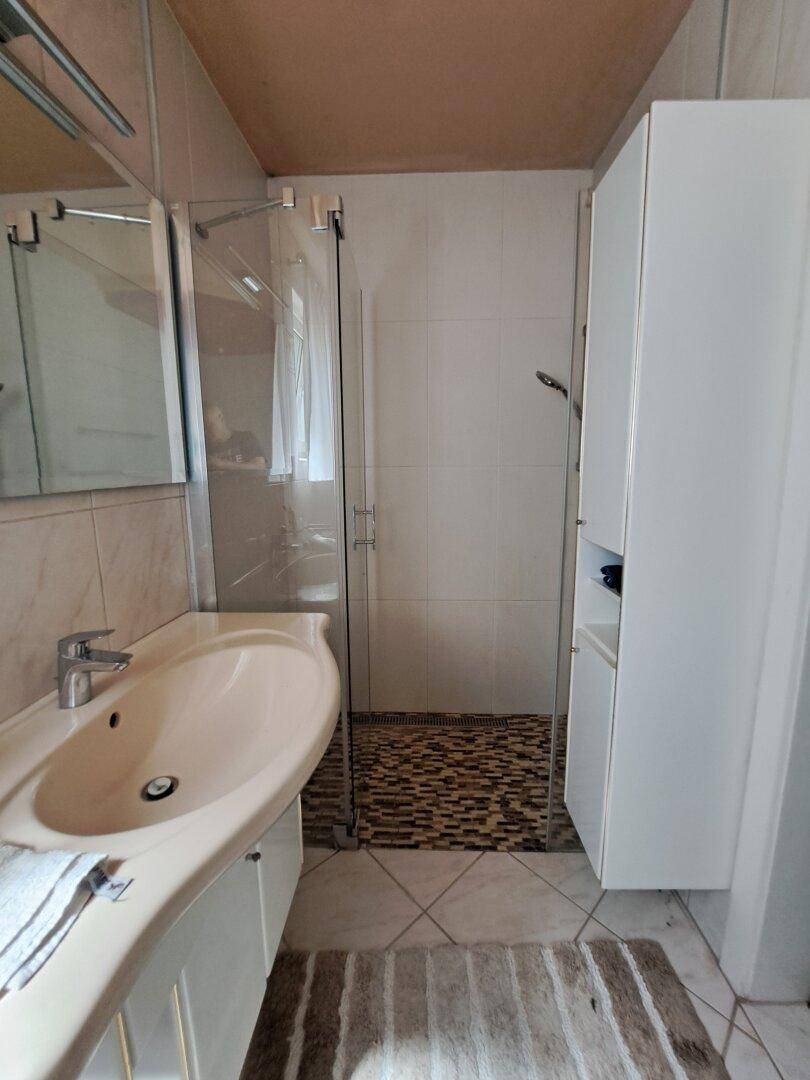 Badezimmer mit Dusche, Waschtisch, Fliesen und Fenster.
