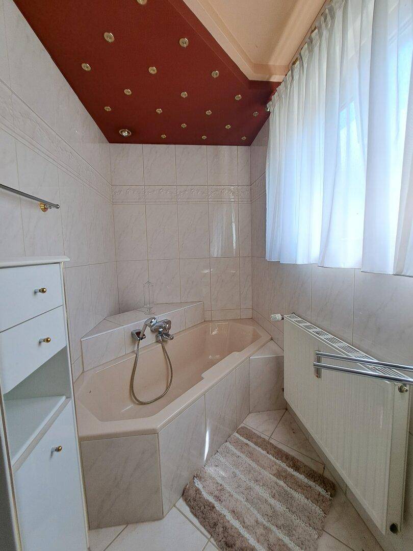 Badezimmer mit Eckbadewanne, Fenster, Fliesen und roter Decke.