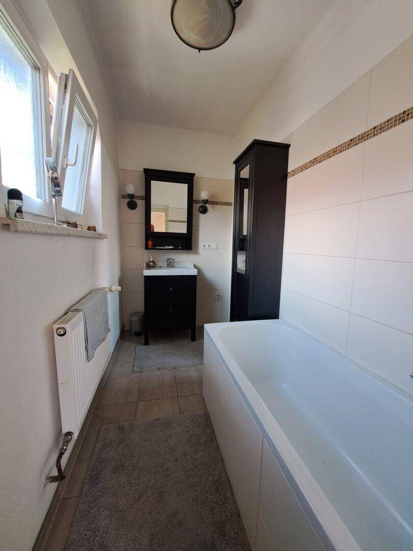 Badezimmer mit Badewanne, Fenster, dunklem Waschtisch und Fliesenboden.