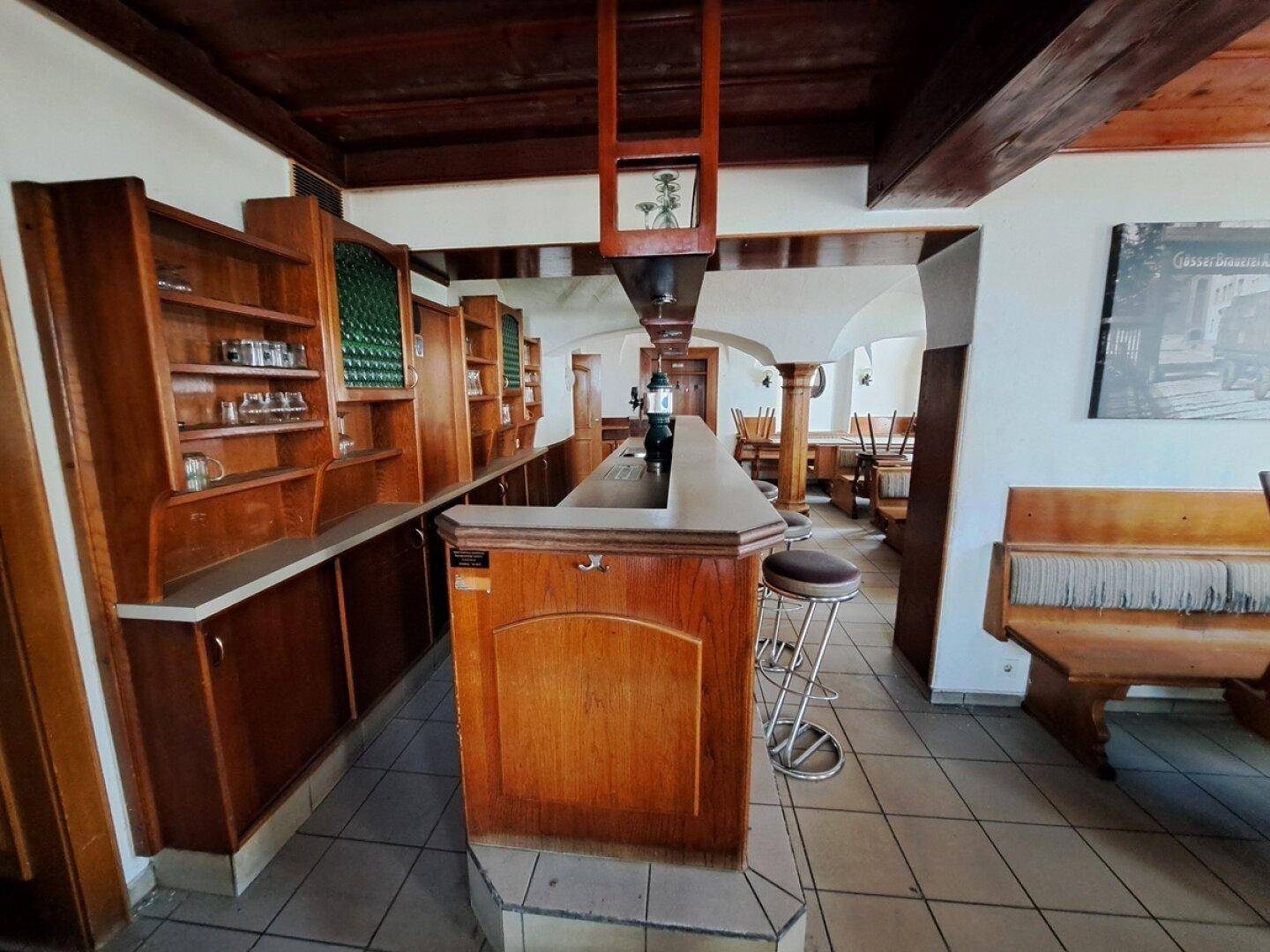 Traditionelle Bar mit Holzelementen, Hockern und gefliestem Boden in einem Gastraum.