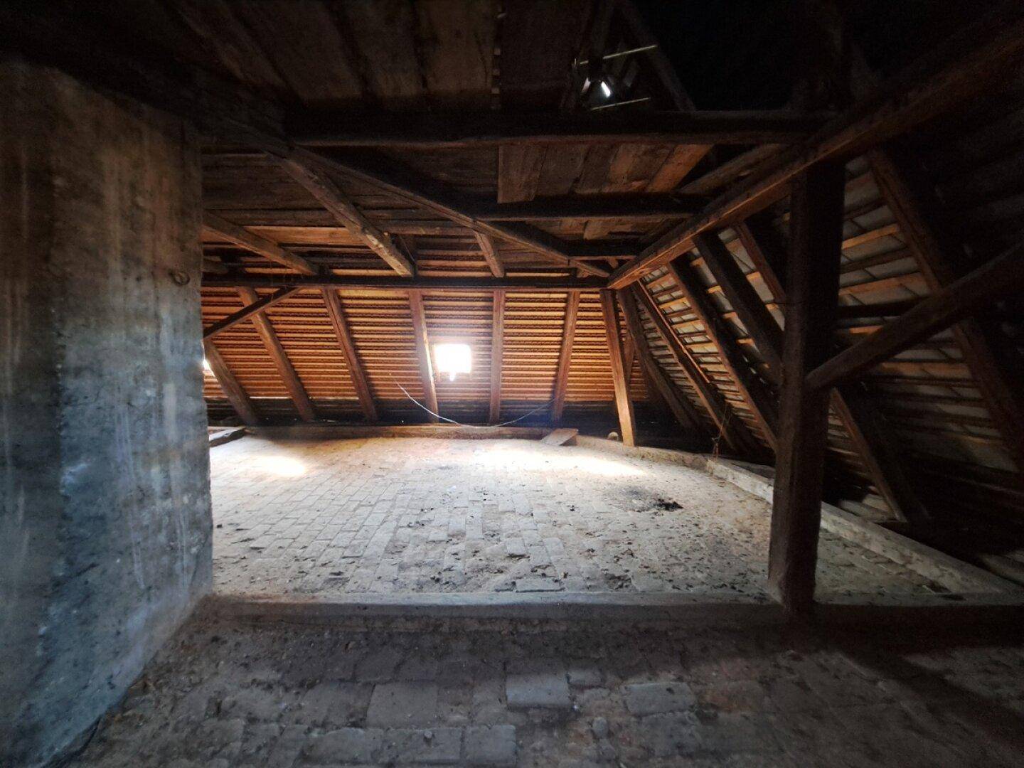 Geräumiger Dachboden mit sichtbaren Holzbalken und Ziegelboden, der viel Potenzial für Ausbau bietet.