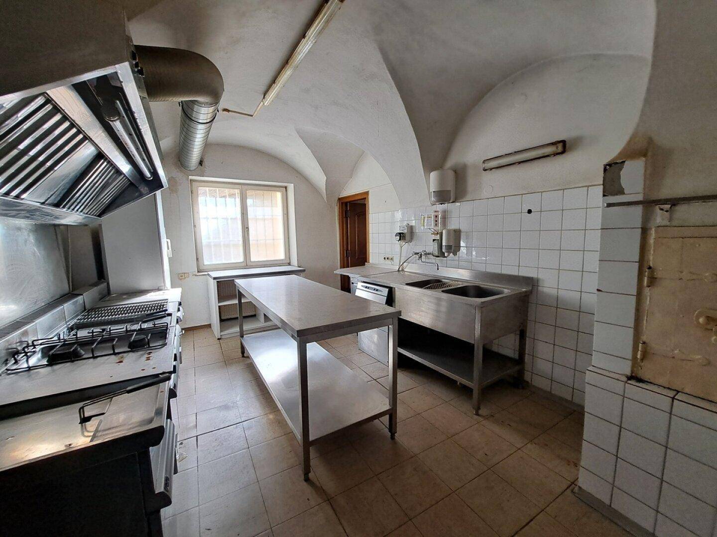Große Gewerbeküche mit Edelstahlgeräten, Gasherd und gewölbter Decke, bereit für den Betrieb.
