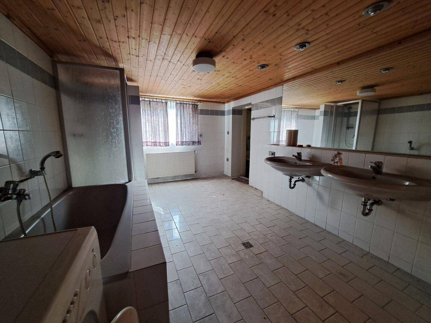 Geräumiges Badezimmer mit Badewanne, Doppelwaschbecken und Holzdecke, das eine Modernisierung benötigt.