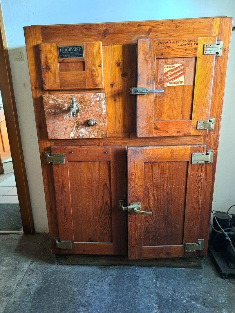 Alter, rustikaler Holz-Eisschrank mit Metallbeschlägen, der an vergangene Zeiten erinnert.