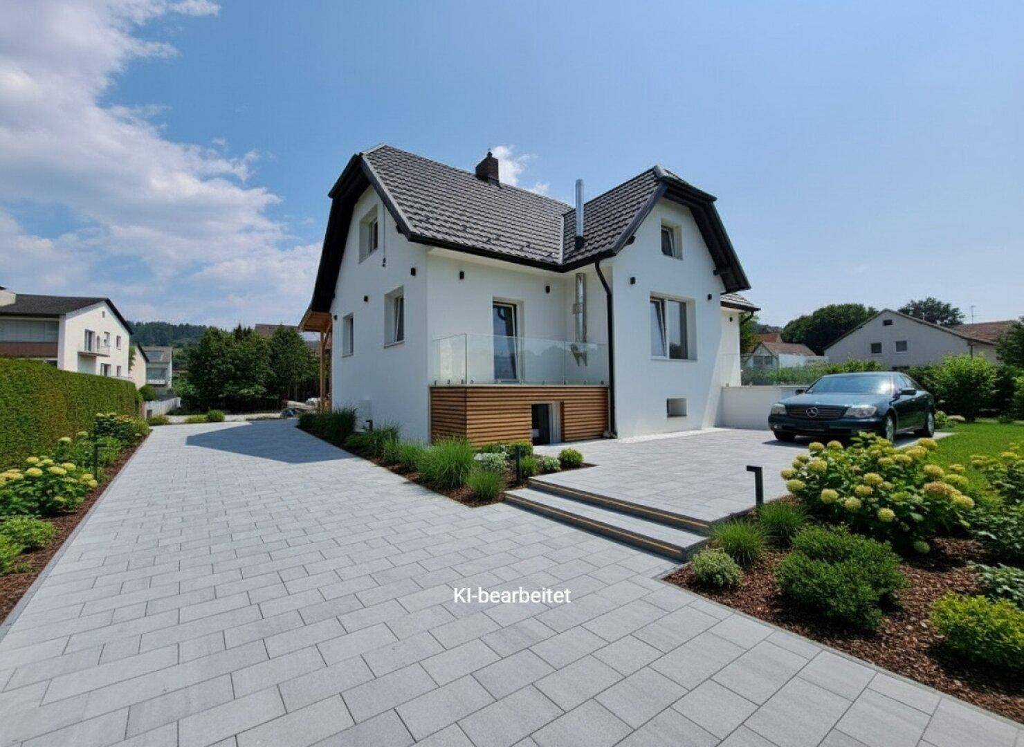 Ansicht des modernen Hauses mit gepflasterter Auffahrt, einem geparkten Auto und grünen Sträuchern.