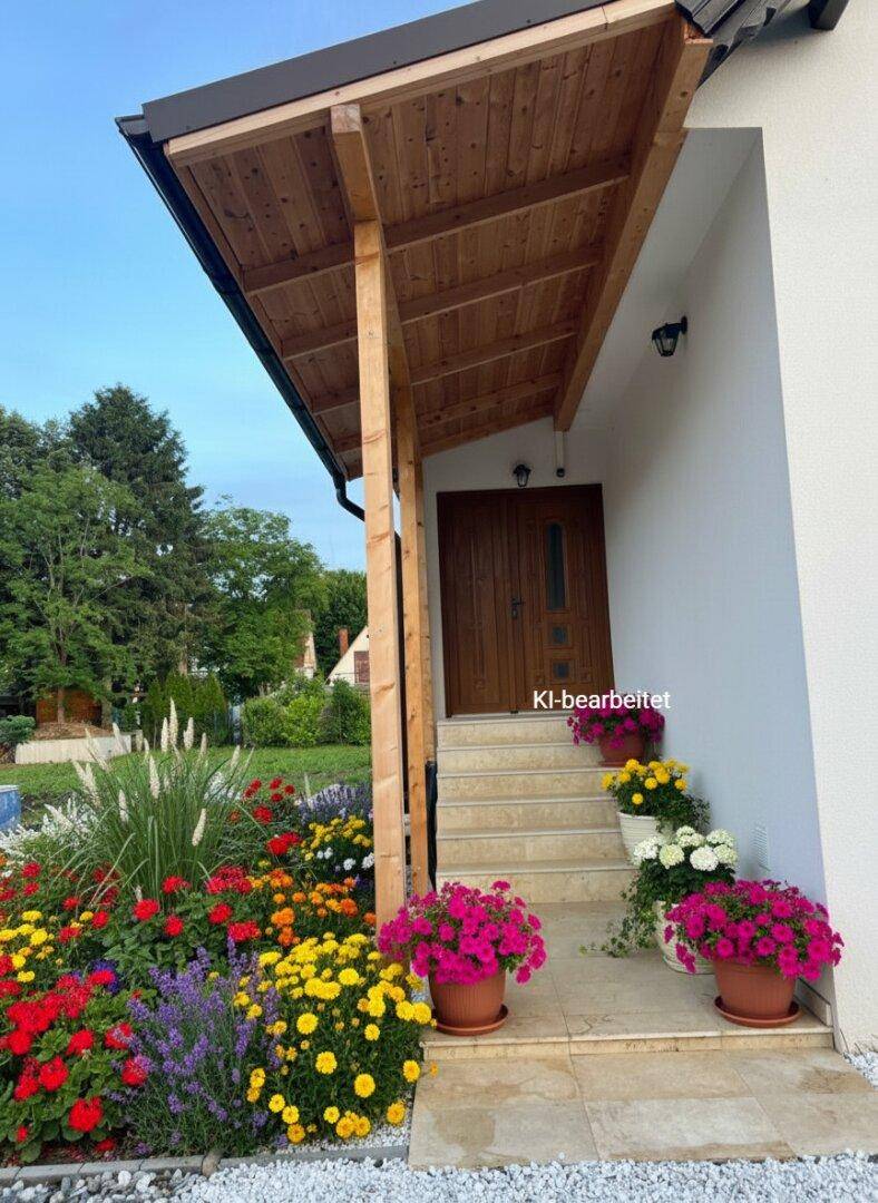 Überdachter Hauseingang mit Holzveranda, Treppe und bunten Blumen in Töpfen und Beeten.