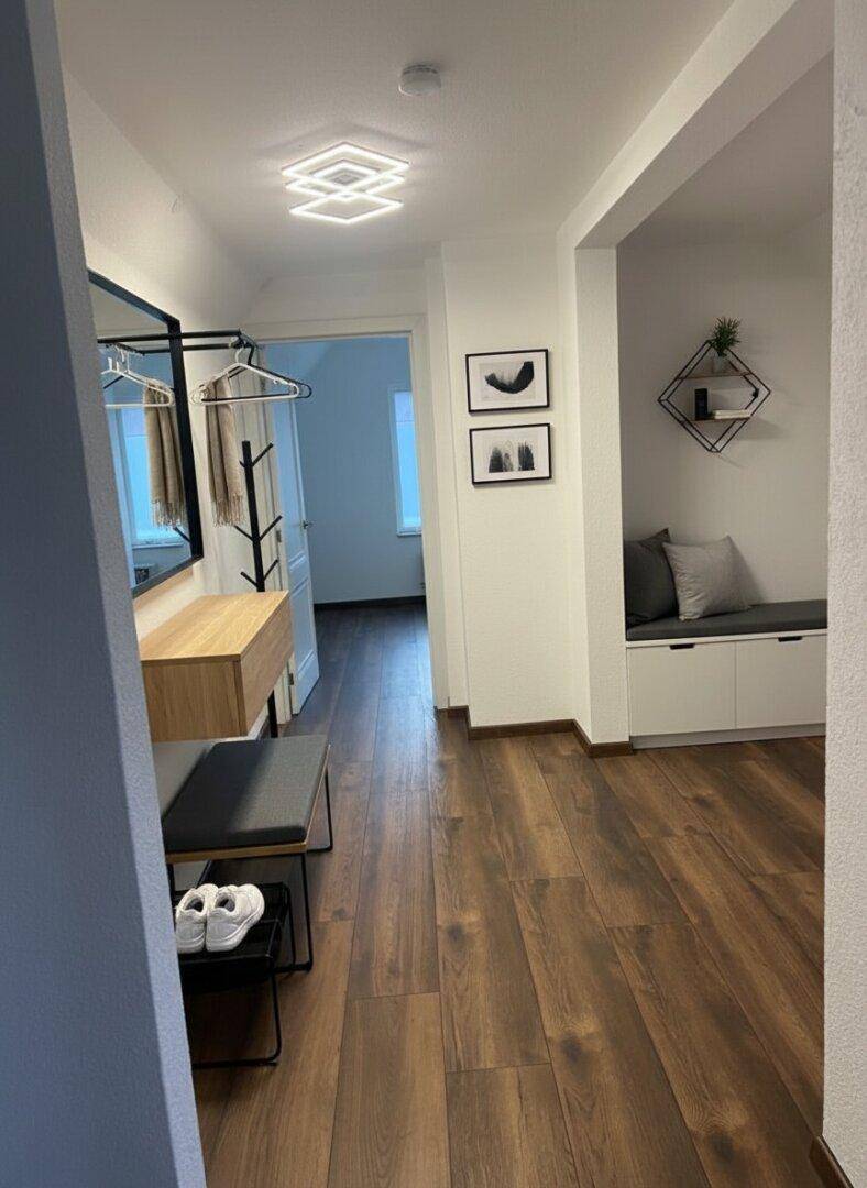Heller Flur mit Garderobe, Spiegel, Sitzbank und dunklem Holzboden.
