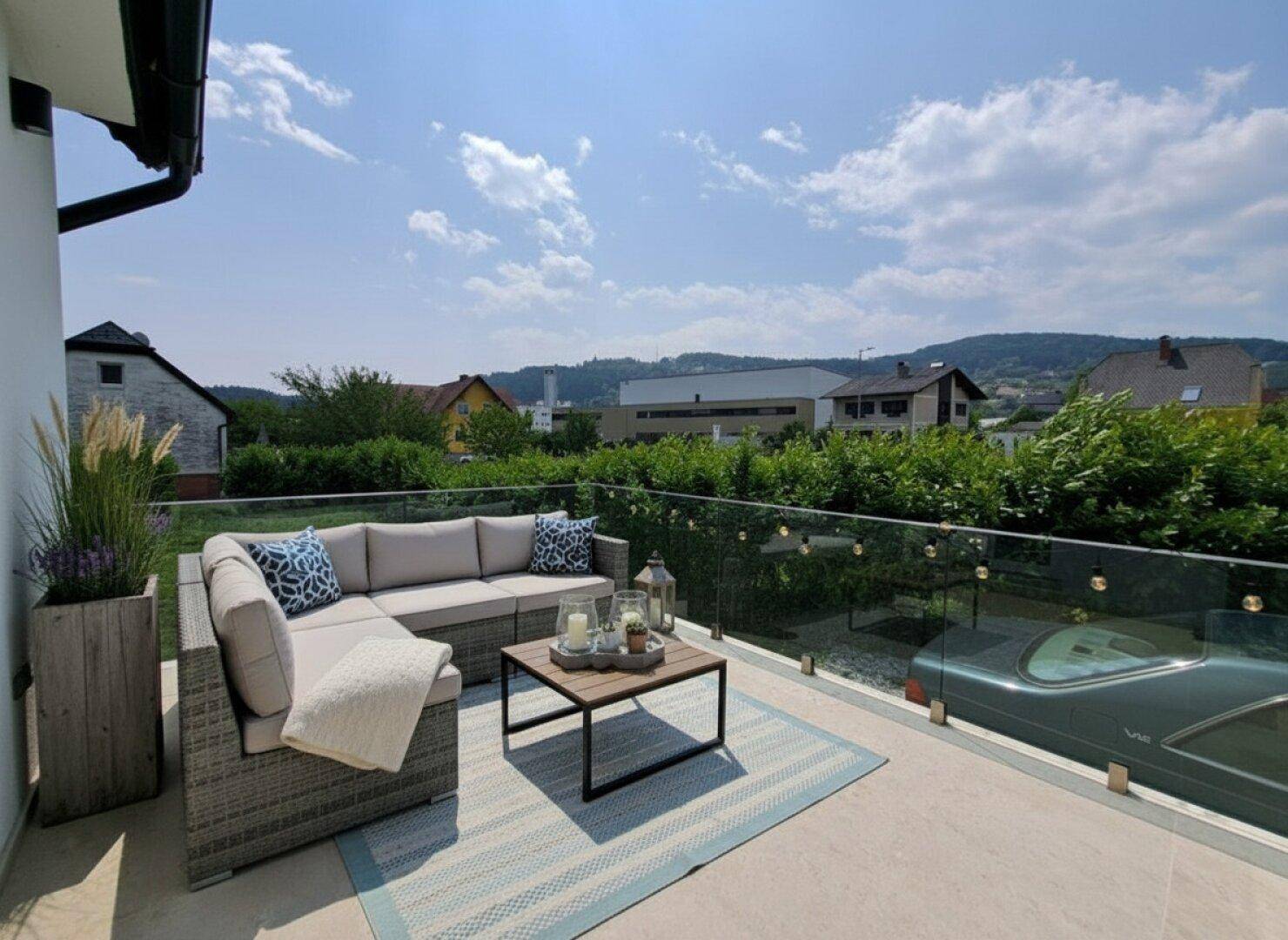 Gemütliche Terrasse mit Loungemöbeln, Teppich und Glasgeländer mit weitem Blick in die Landschaft.
