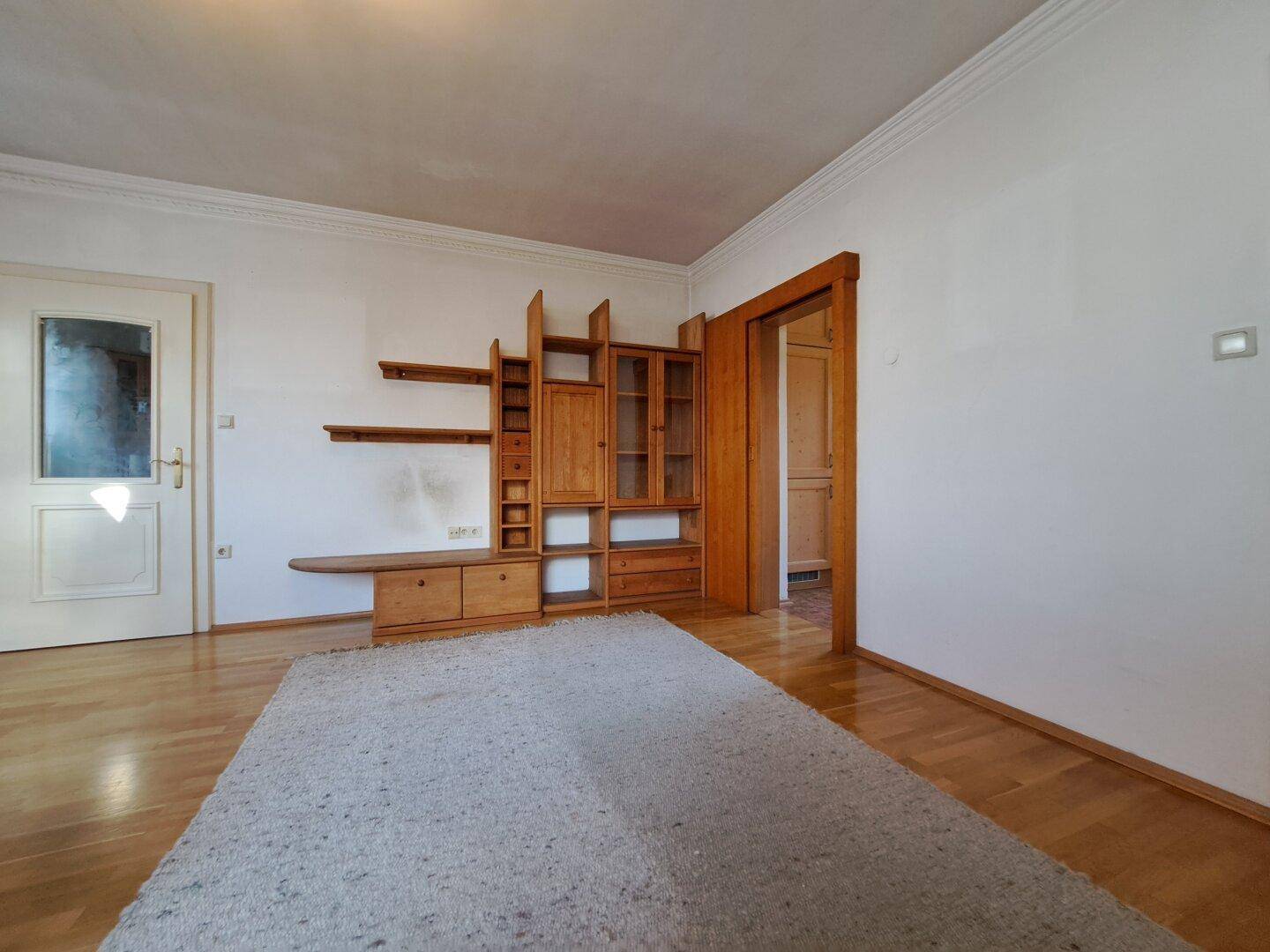 Wohnbereich mit Parkettboden, Teppich und rustikalem Holzregalsystem.