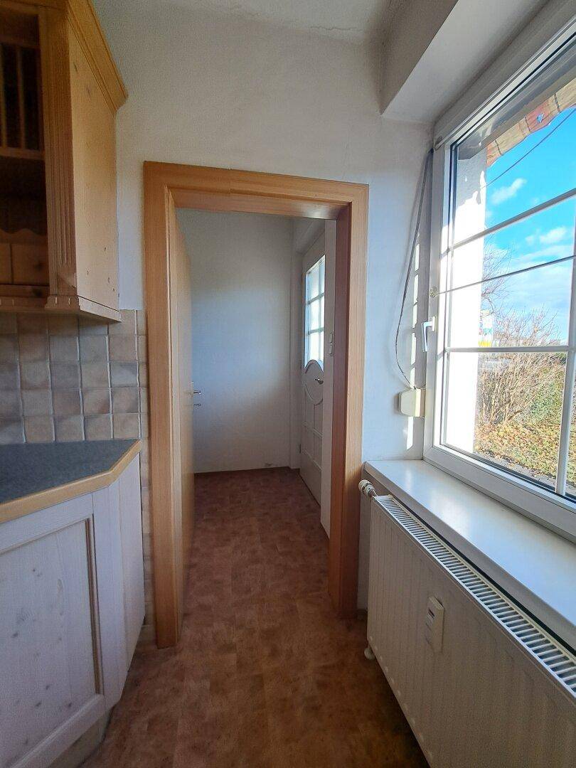 Heller Küchenflur mit Fenster und Zugang zu weiteren Räumen.