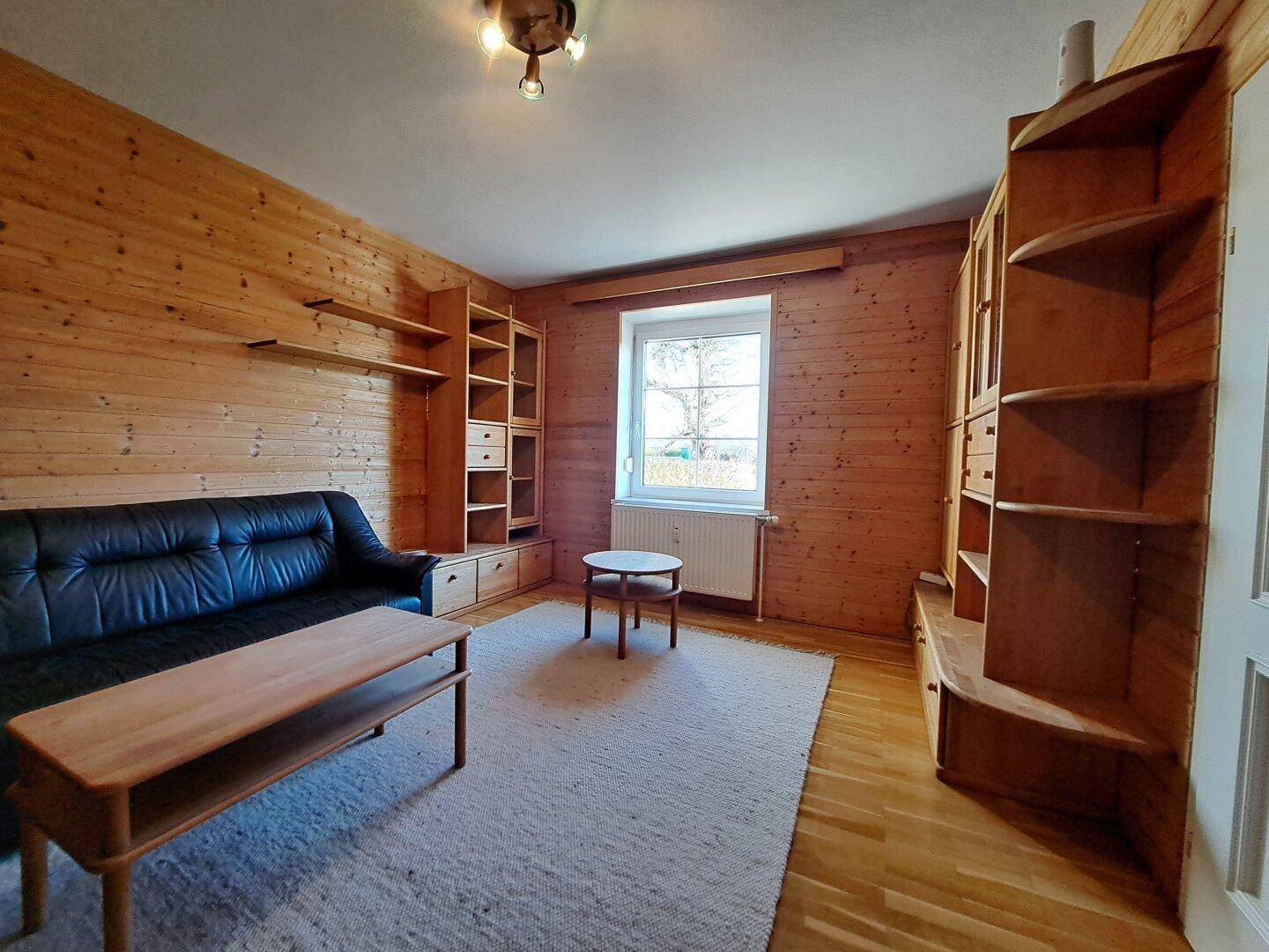 Wohnzimmer mit Holzwänden, Sofa, Couchtisch und Regalsystem.