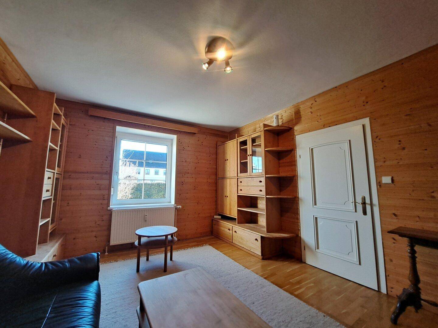 Wohnzimmer mit Holzverkleidung, Fenster und hellem Parkettboden.