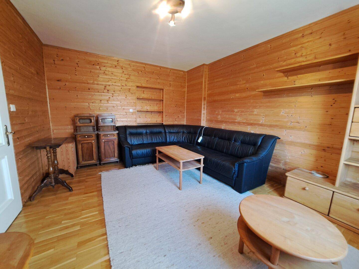 Geräumiges Wohnzimmer mit Holzwänden, großem Ecksofa und Holztischen.