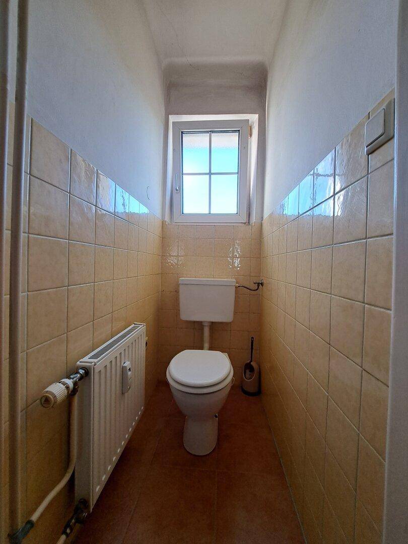 Separates WC mit Fenster, beigefarbenen Fliesen und Heizkörper.