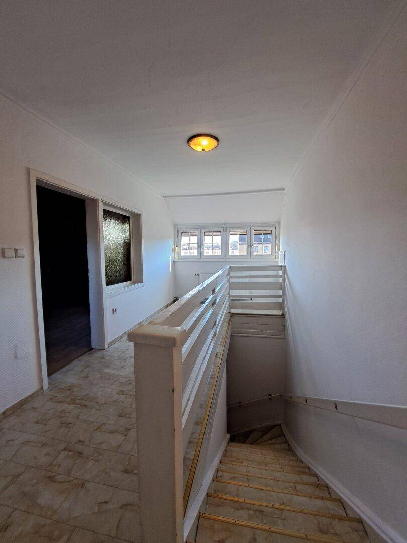 Heller Flur mit Treppenaufgang, Fliesenboden und Fenstern im Obergeschoss.