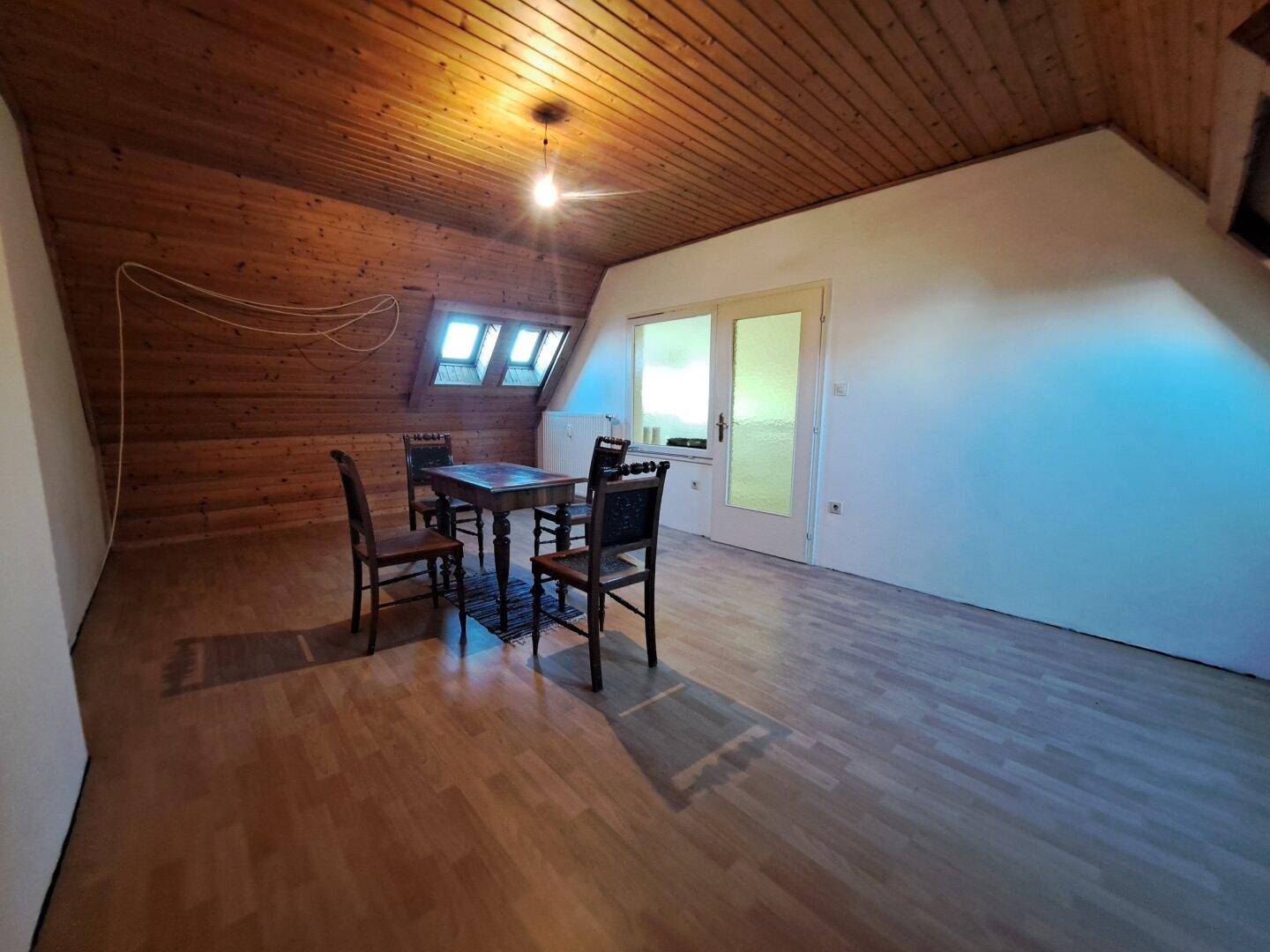 Geräumiger Dachbodenraum mit schräger Holzdecke, Holzboden und Tischgruppe.