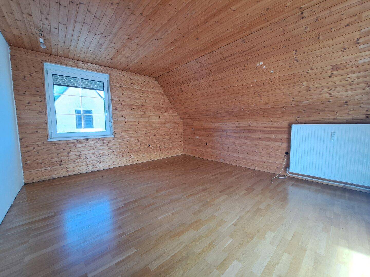 Heller Dachbodenraum mit Holzverkleidung, Holzboden und Fenster.