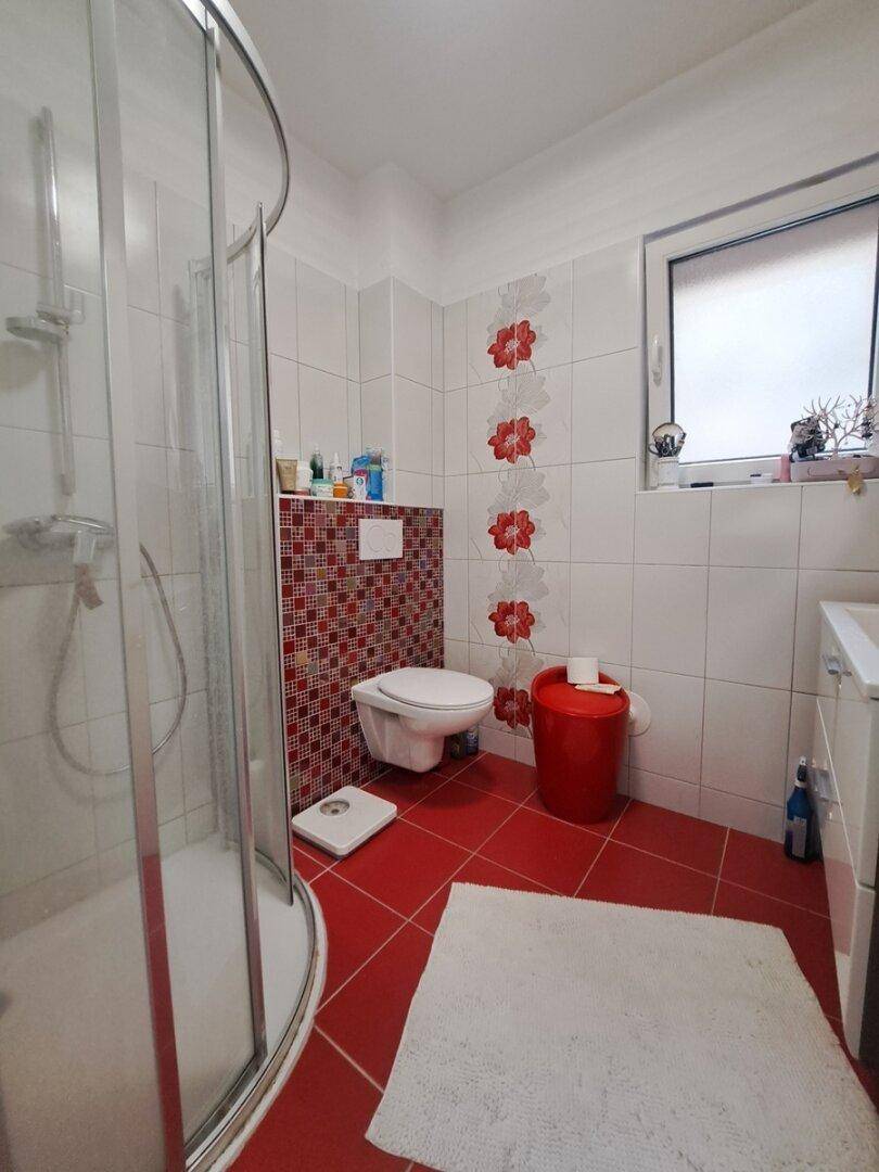 Badezimmer mit Duschkabine, roten Fliesen und einem Fenster für natürliche Belüftung und Licht.