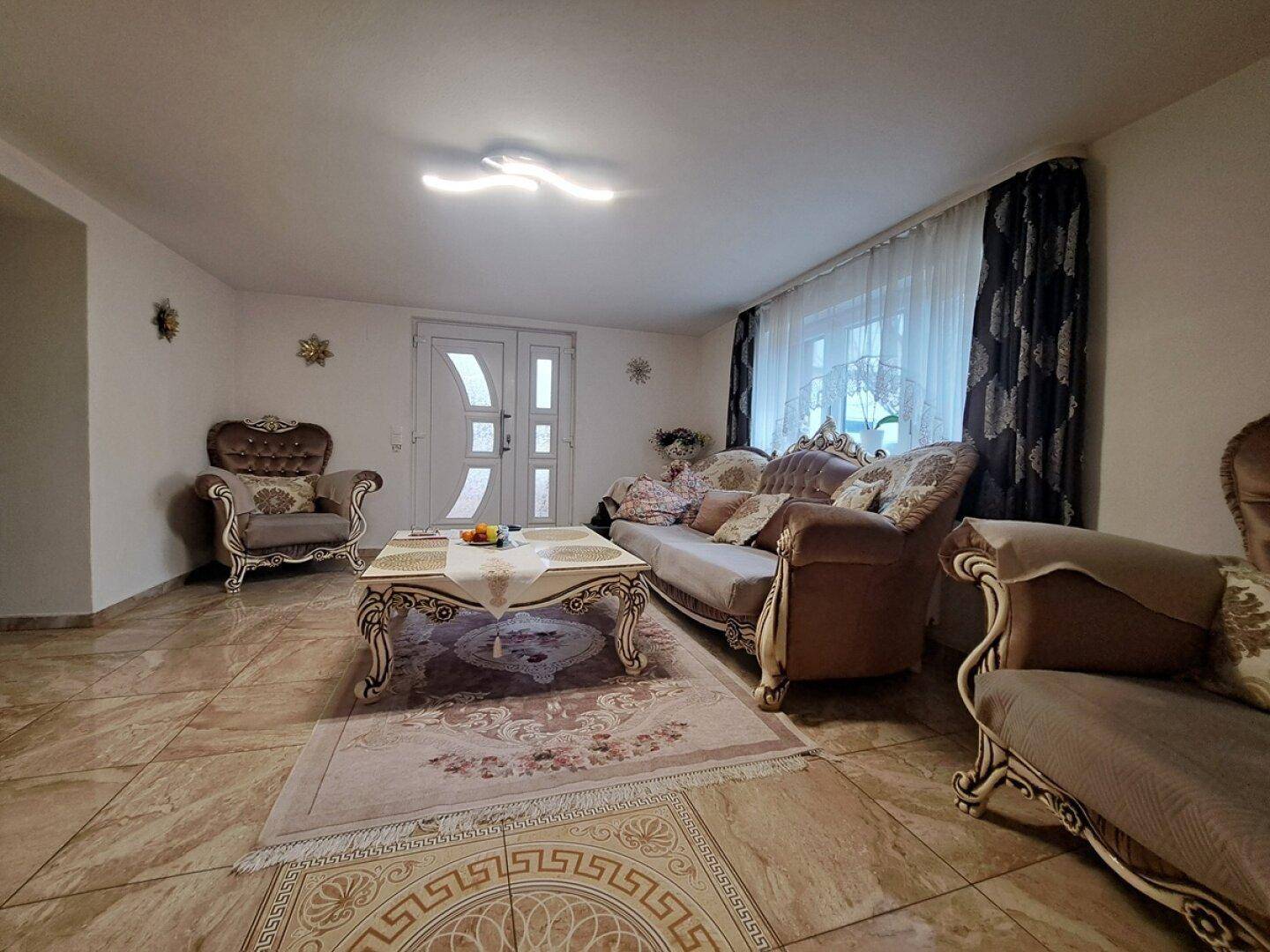 Gemütliches Wohnzimmer mit gefliestem Boden, eleganten Möbeln und großen Fenstern für viel Tageslicht.