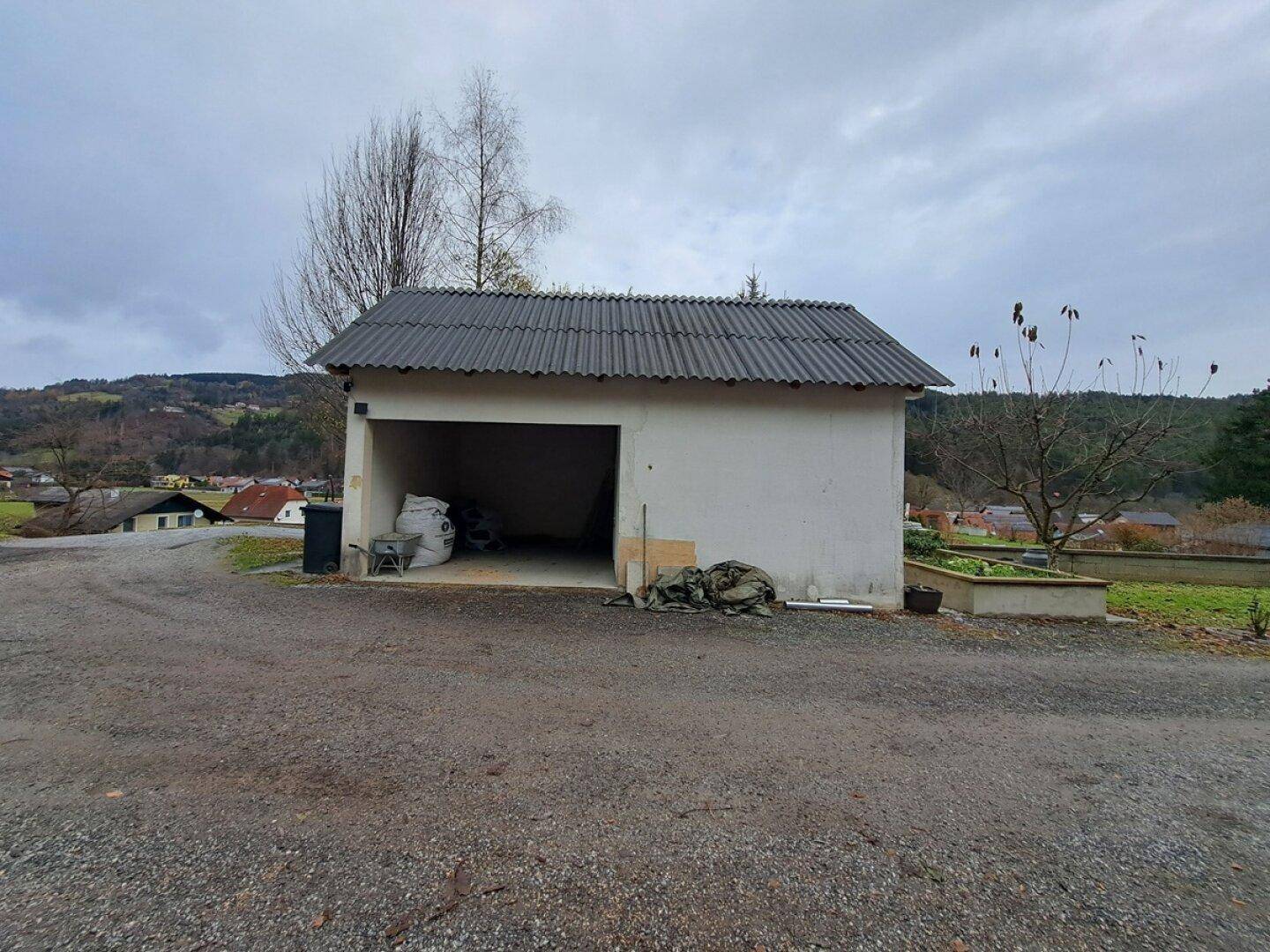 Freistehende Garage mit offenem Zugang und Schrägdach in einer ländlichen Umgebung.