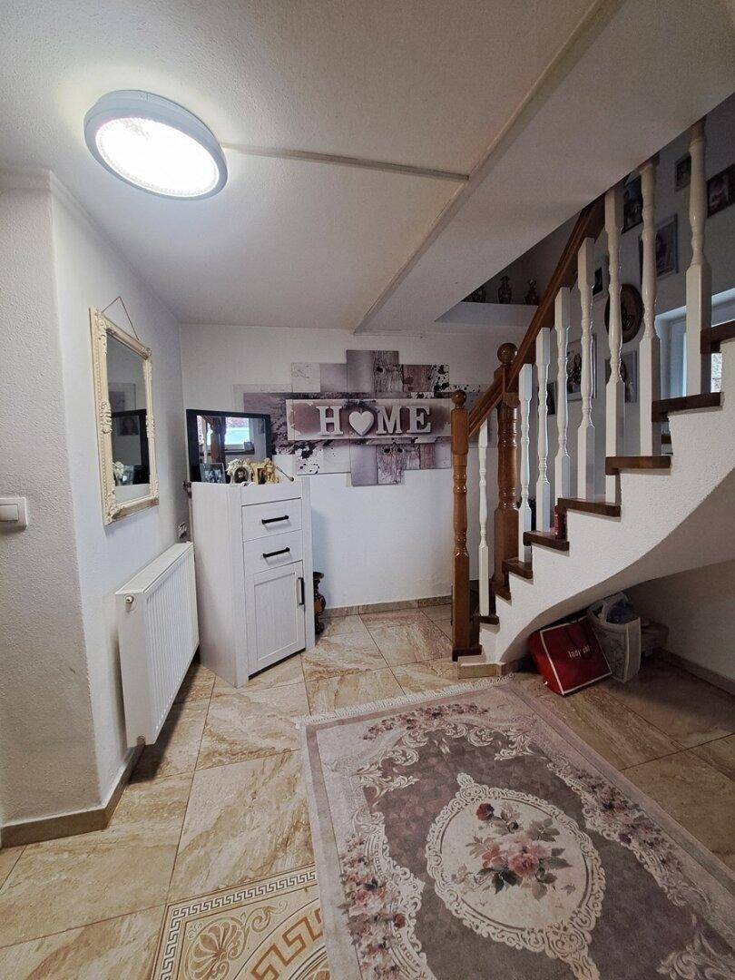 Eingangsbereich mit gefliestem Boden, geschwungener Holztreppe und dekorativem Spiegel an der Wand.