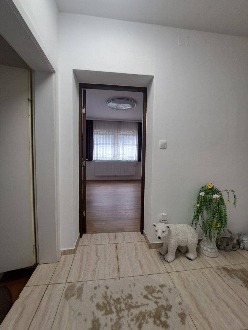 Heller Flur mit gefliestem Boden und Durchgang zu einem angrenzenden Zimmer mit Laminatboden.