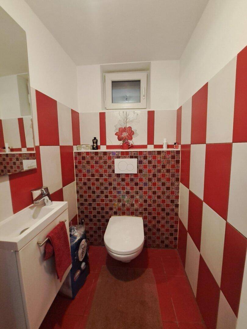 Kleines Gäste-WC mit auffälligen rot-weißen Fliesen, einem Fenster und modernem Wand-WC.